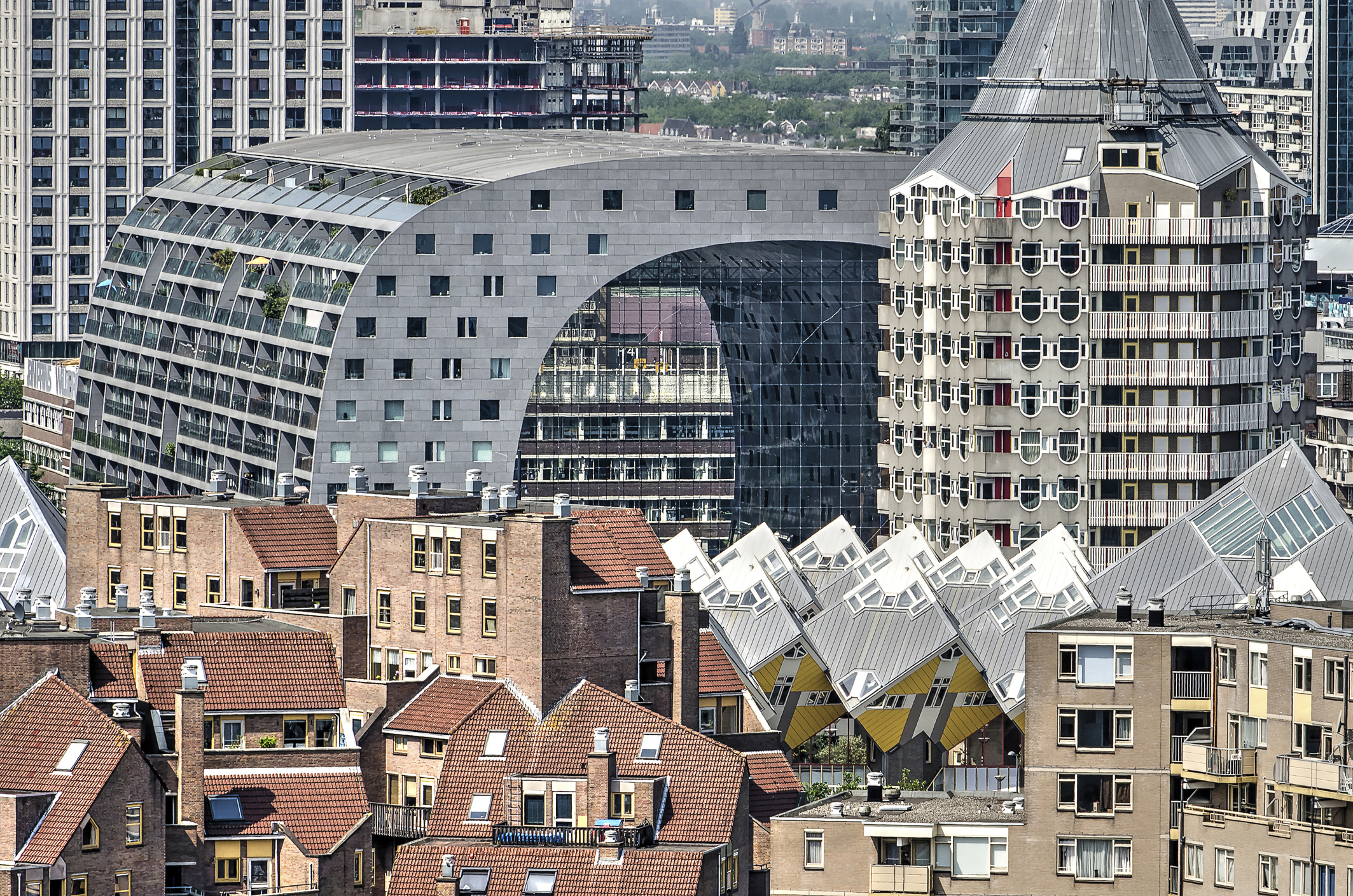Cityscape of Rotterdam, Netherlands, featuring the iconic Markthal building with its arch-shaped structure, the Cube Houses with tilted yellow roofs, and the Pencil Tower surrounded by traditional brick residential buildings.